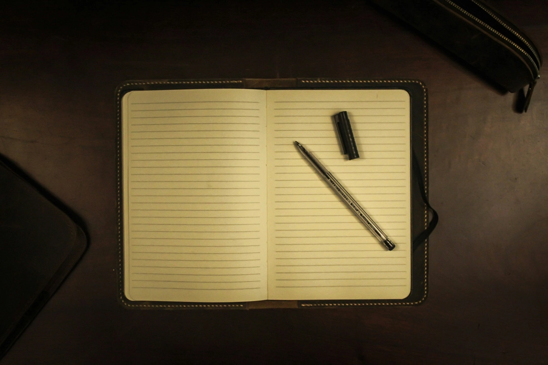 Open notebook with a pen on a dark wooden desk, symbolizing the initial steps on how to set up Python logging module with file handlers and message formatting.