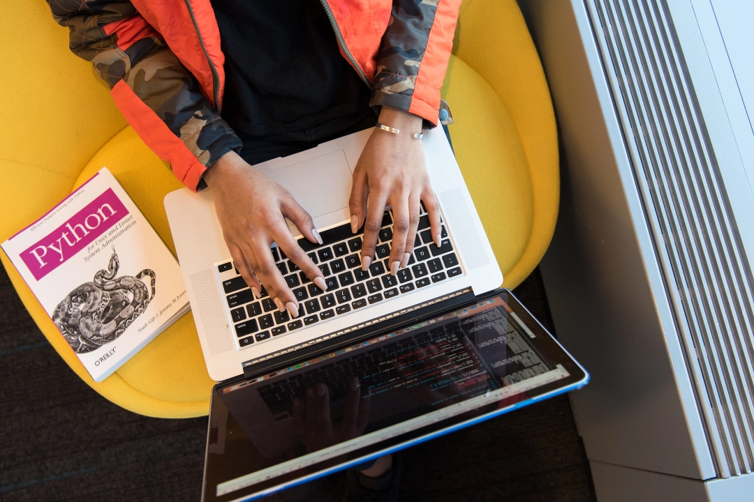 A person typing on a laptop with a Python programming book beside them, symbolizing the concept of understanding Python metaclasses for advanced class customization.