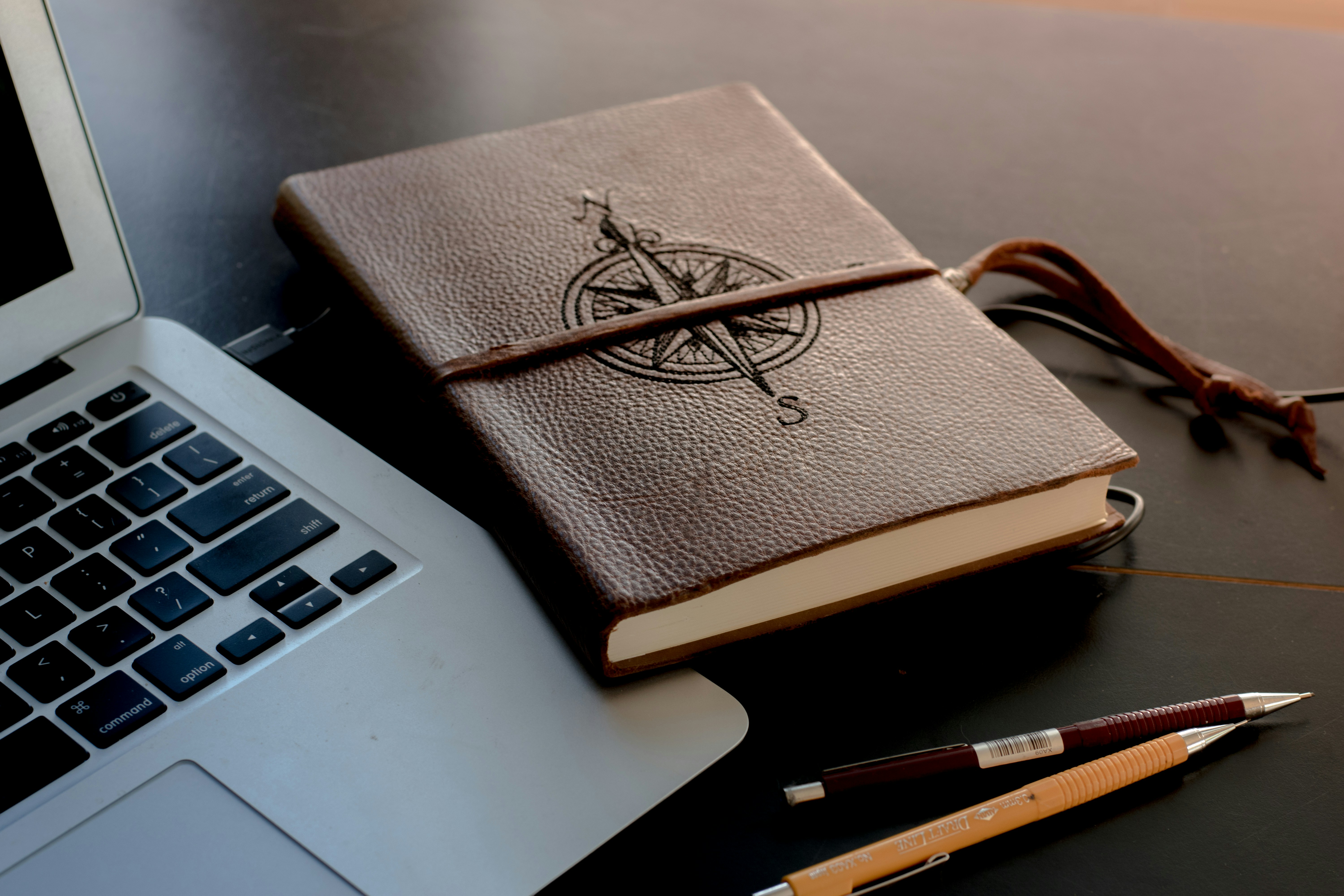 Leather-bound journal with compass emblem next to a laptop and pens, symbolizing meticulous project planning using advanced Python logging configuration techniques for improved maintenance.
