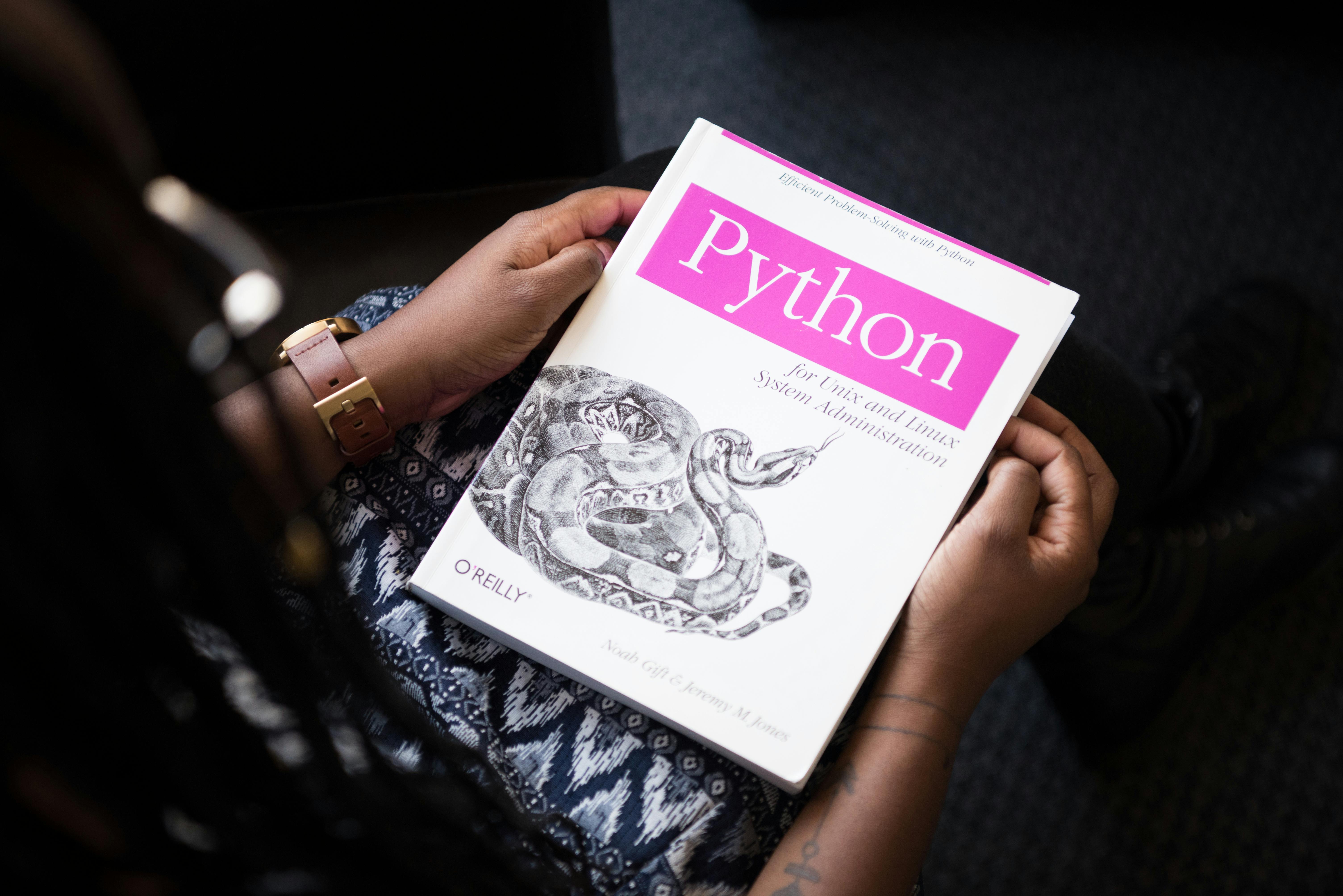 A person holding a Python book titled "Python for Unix and Linux System Administration" by Noah Gift and Jeremy Jones, showcasing the importance of learning best practices for improving Python programming skills.