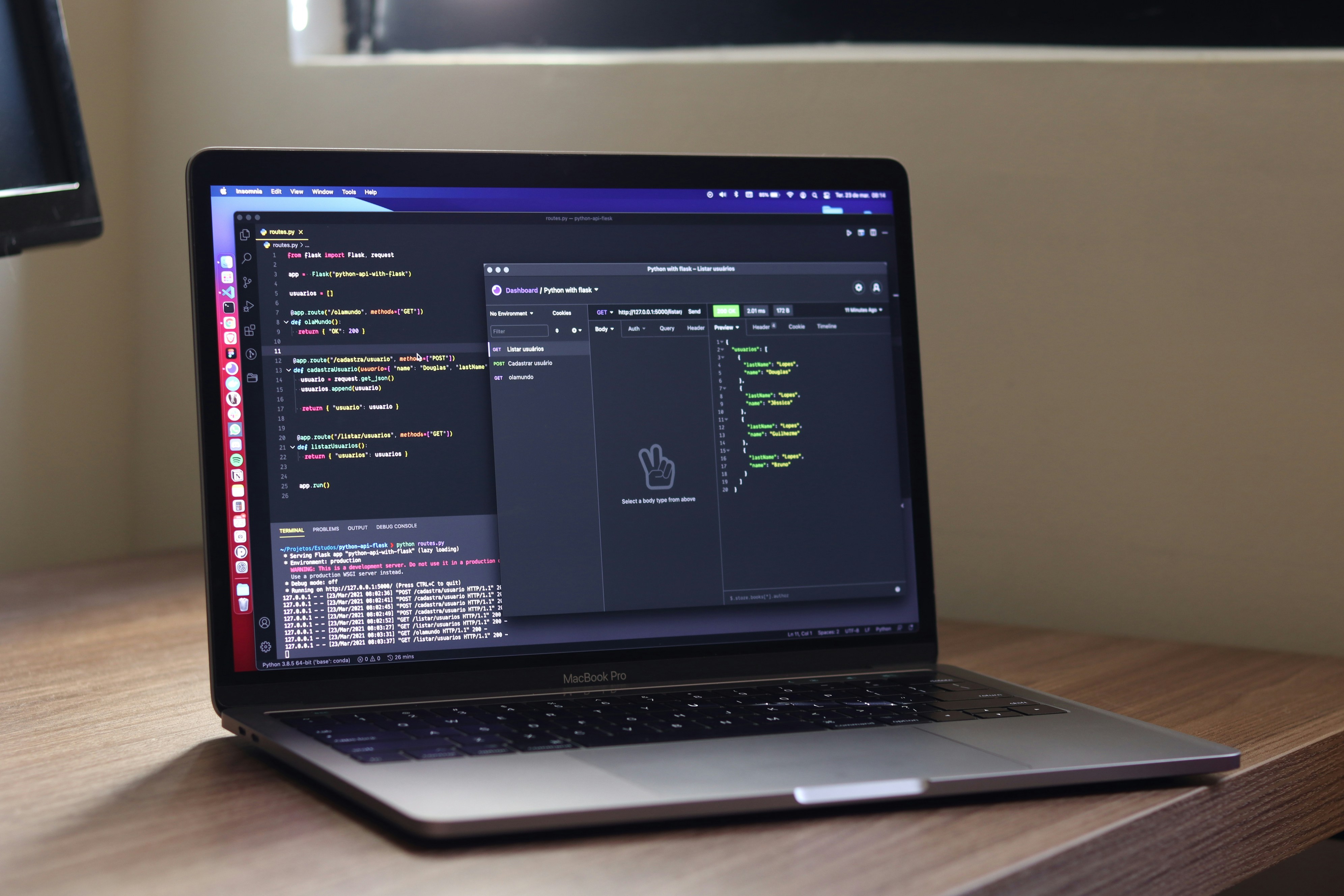 MacBook Pro on a desk displaying code from a 'Building REST APIs with Python and FastAPI tutorial' on screen with API testing application Postman in view.