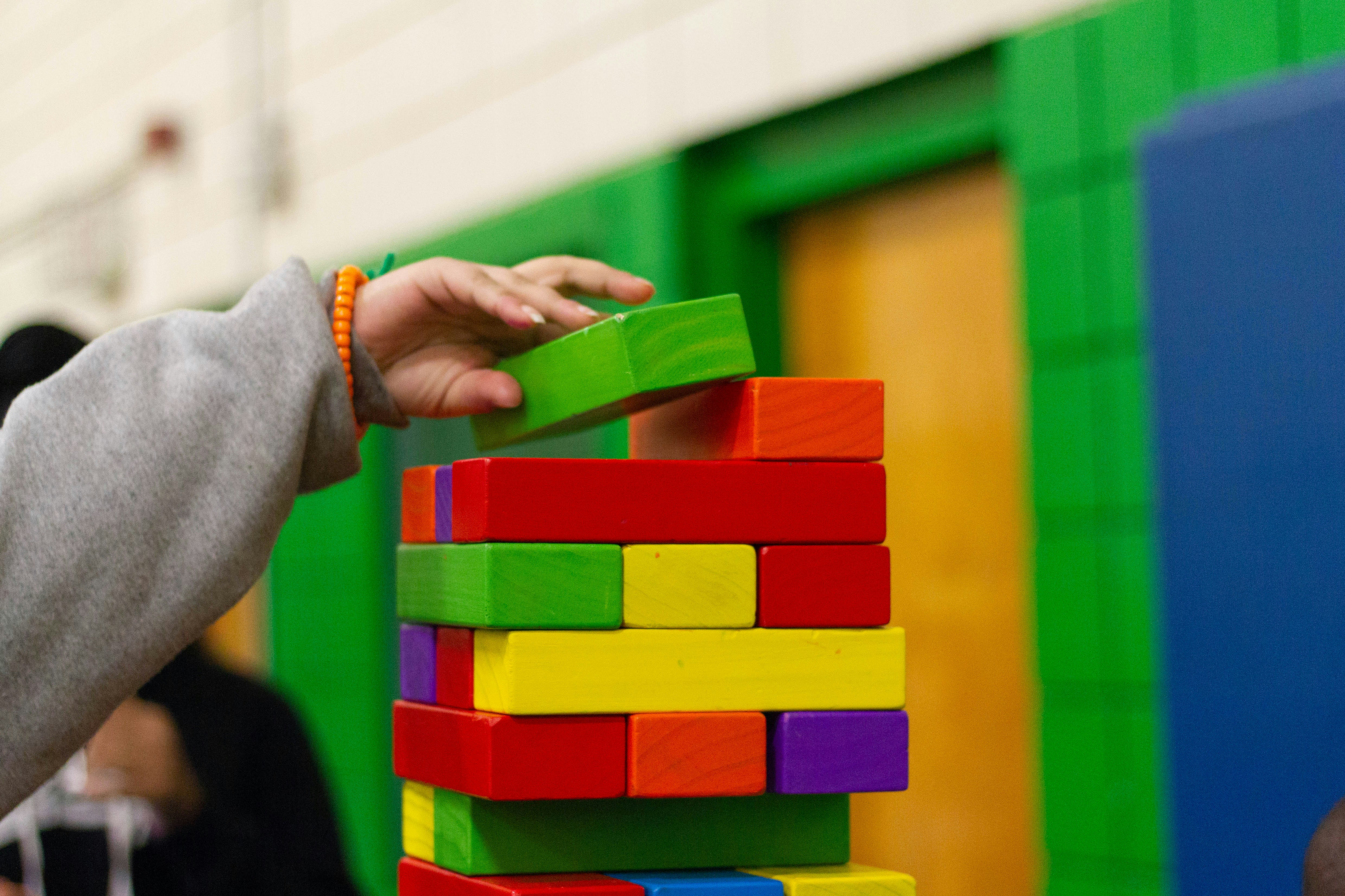 Hand stacking colorful wooden blocks, symbolizing composition over inheritance in software development for building scalable systems.