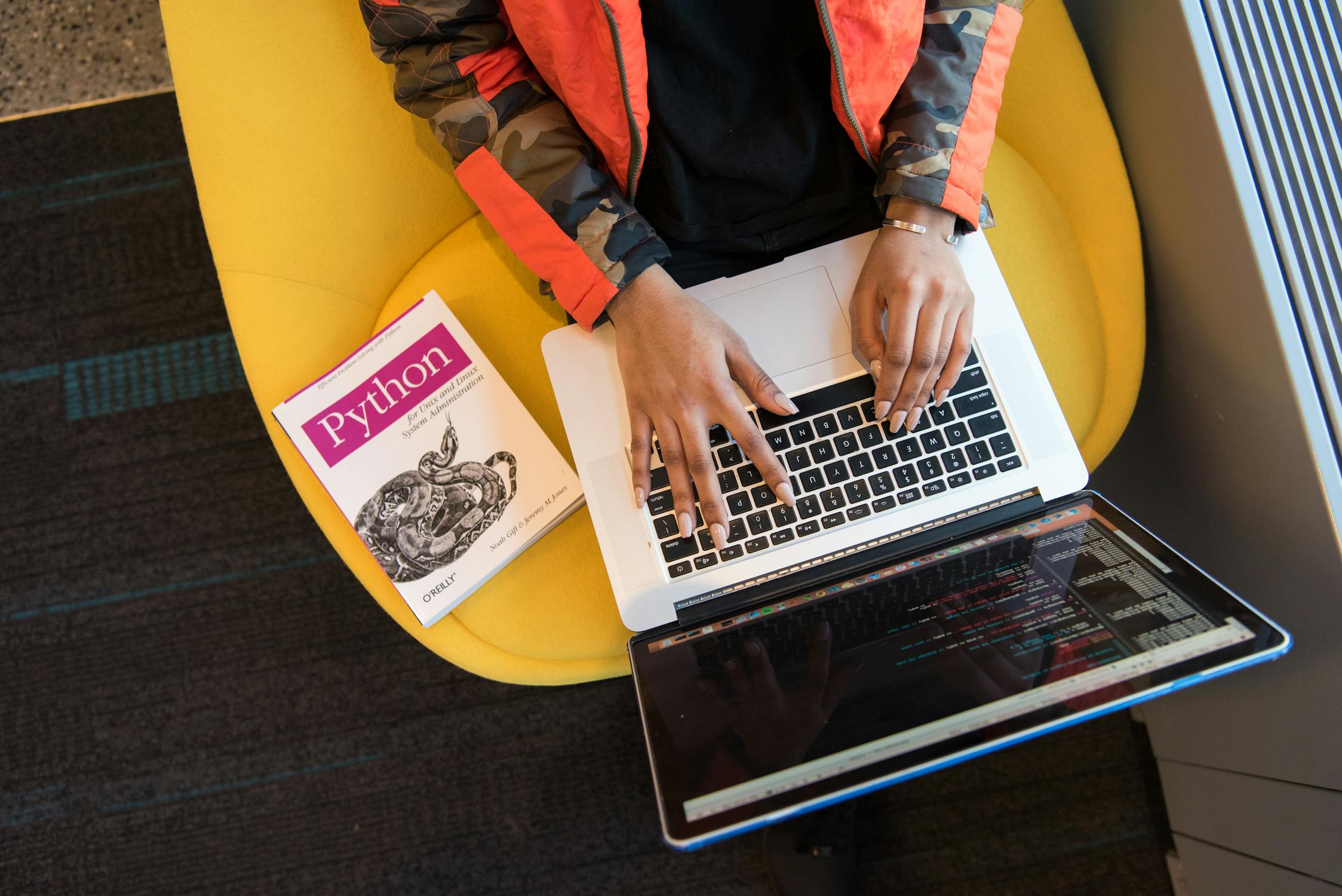 Programmer using a laptop with code on screen, next to a Python programming book, illustrating effective strategies for refactoring legacy code.