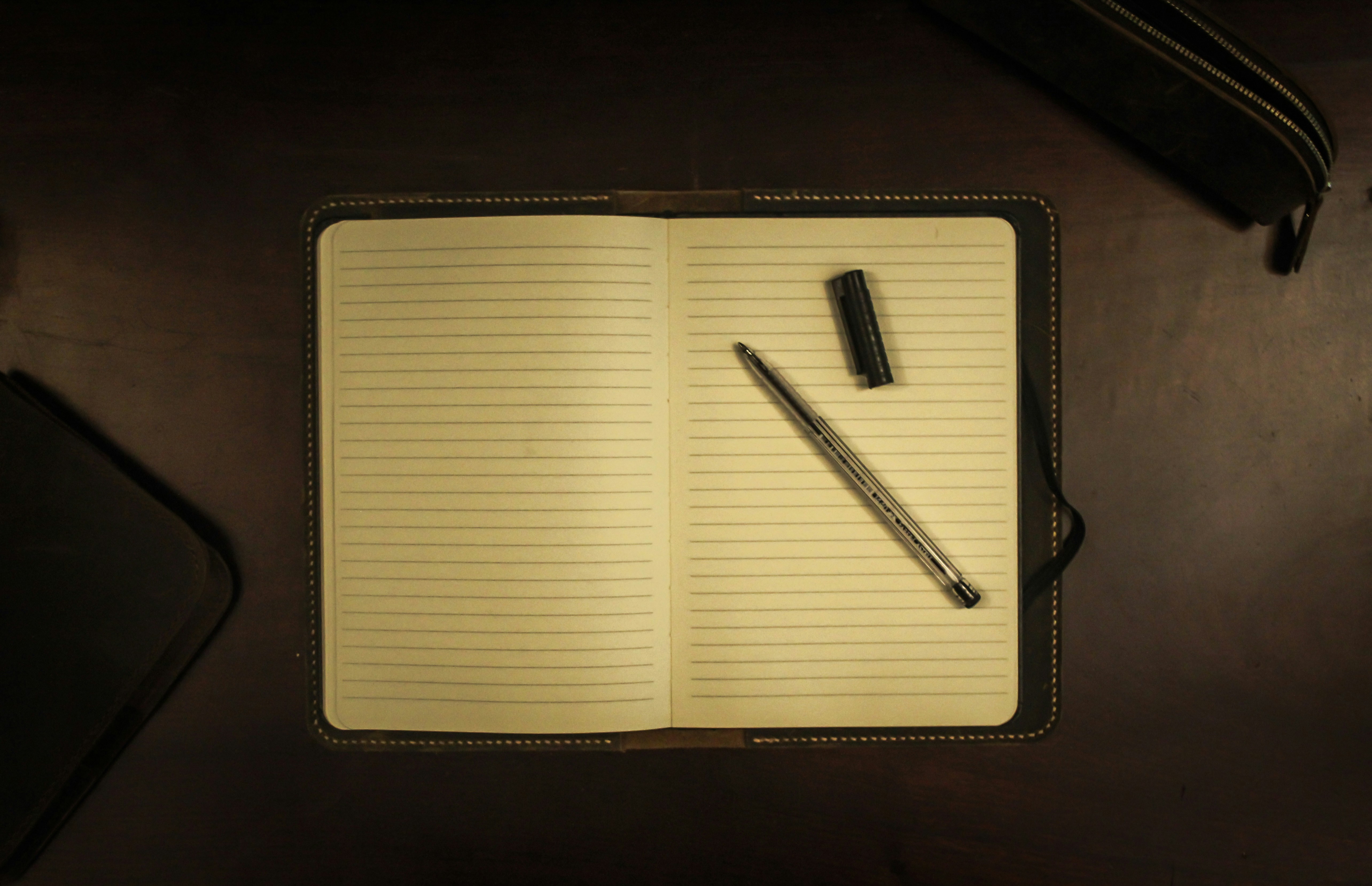 Open notebook with a pen on a dark wooden desk, symbolizing the initial steps on how to set up Python logging module with file handlers and message formatting.
