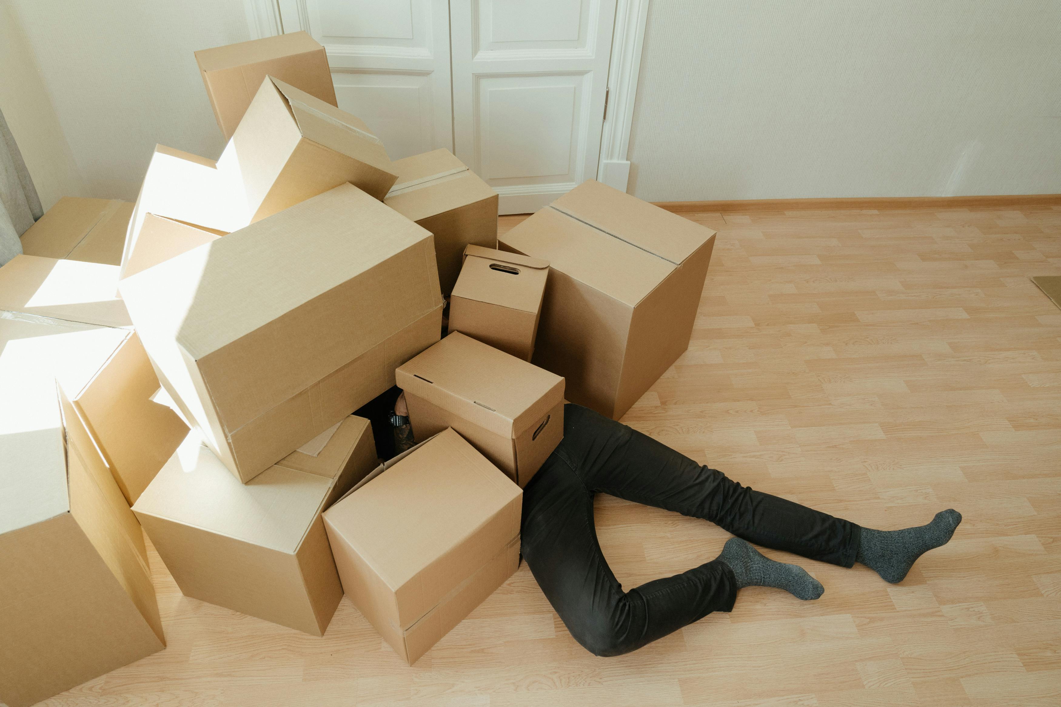 A person overwhelmed by a heap of cardboard boxes while unpacking or packing, symbolizing the importance of learning best practices for organizing Python code with packages and modules for efficient workflow.