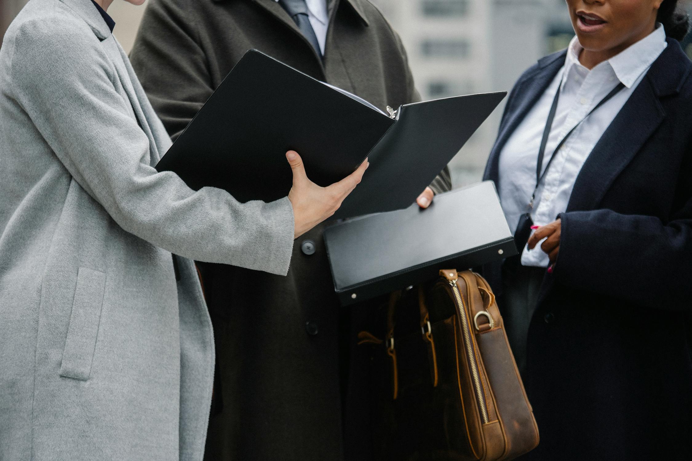 Three professionals in business attire discussing documents, with the focus on a person holding a folder, symbolizing the teamwork and strategic-thinking needed in a senior developer role.