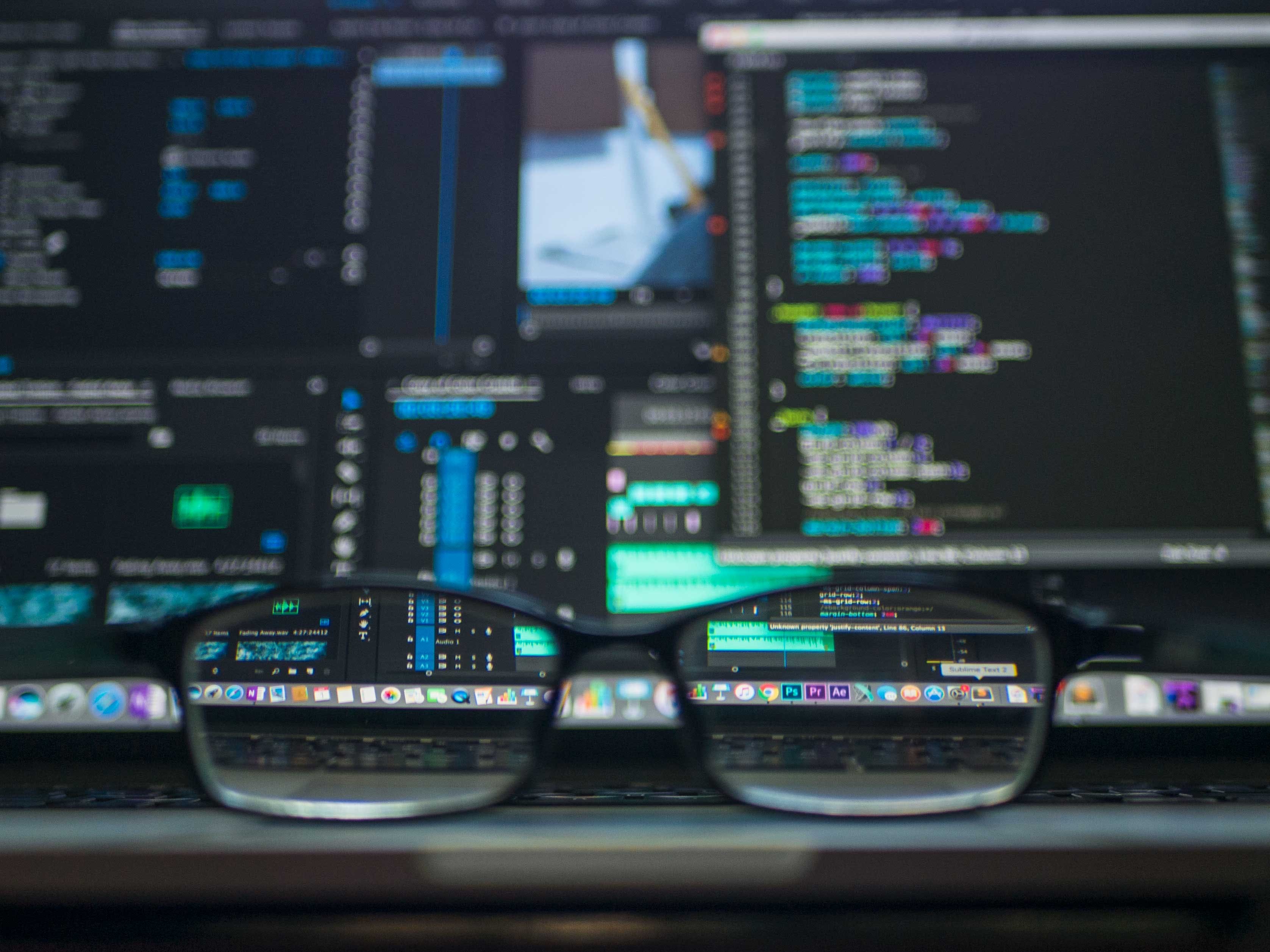 Close-up of eyeglasses focused on computer screens displaying code, illustrating the concept of Python functors and monads for efficient programming.